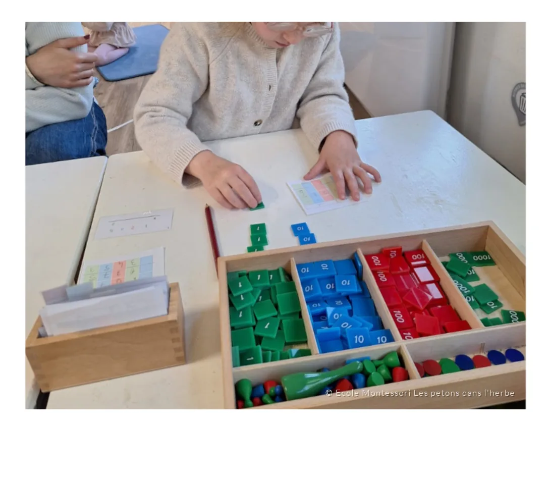 Les mains d’un enfant manipulent les timbres Montessori des unités, dizaines, centaines et milliers.