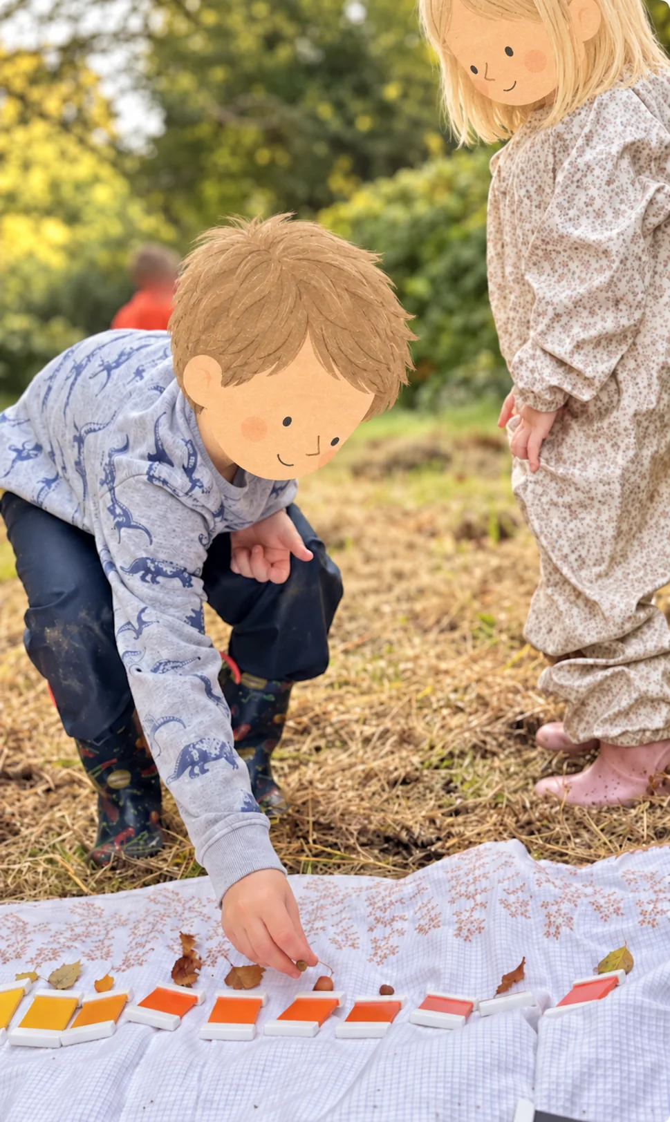 Un enfant associe une feuille à une tablette de couleur dehors. Les têtes des deux enfants sont dessinées sur la photographie.